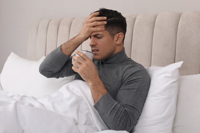 Photo of Sick man with cup of hot drink in bed at home