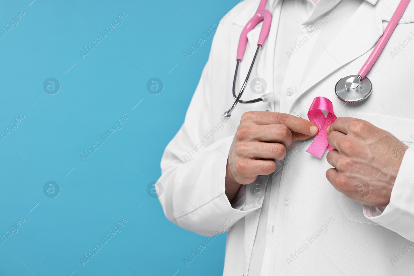 Photo of Mammologist with pink ribbon and stethoscope on light blue background, closeup. Space for text