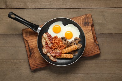 Photo of Frying pan with cooked traditional English breakfast on wooden table, top view