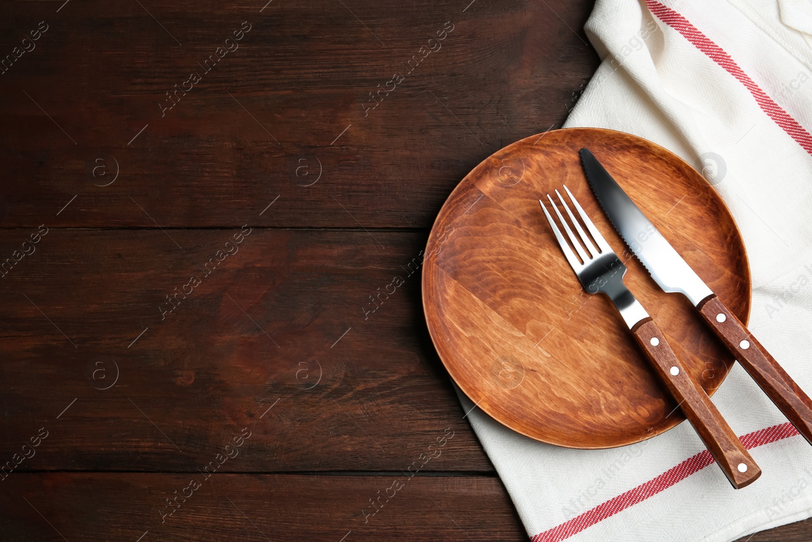 Photo of Plate with cutlery and white fabric on wooden table, flat lay. Space for text