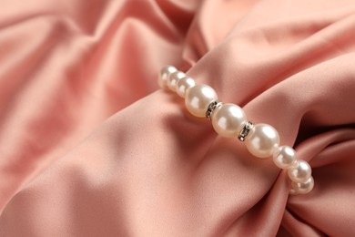 Photo of Elegant bracelet with pearls on pink silk, closeup