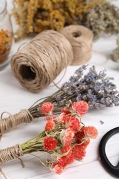 Photo of Bunches of dry flowers, different medicinal herbs and spools on white wooden table