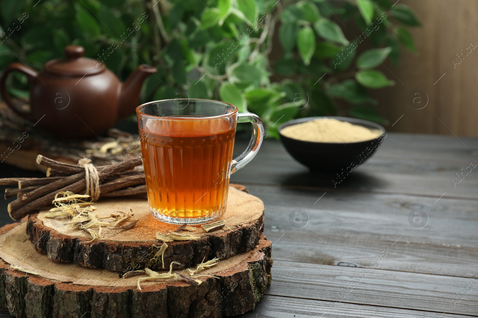 Photo of Aromatic licorice tea in cup and dried sticks of licorice root on black wooden table, space for text