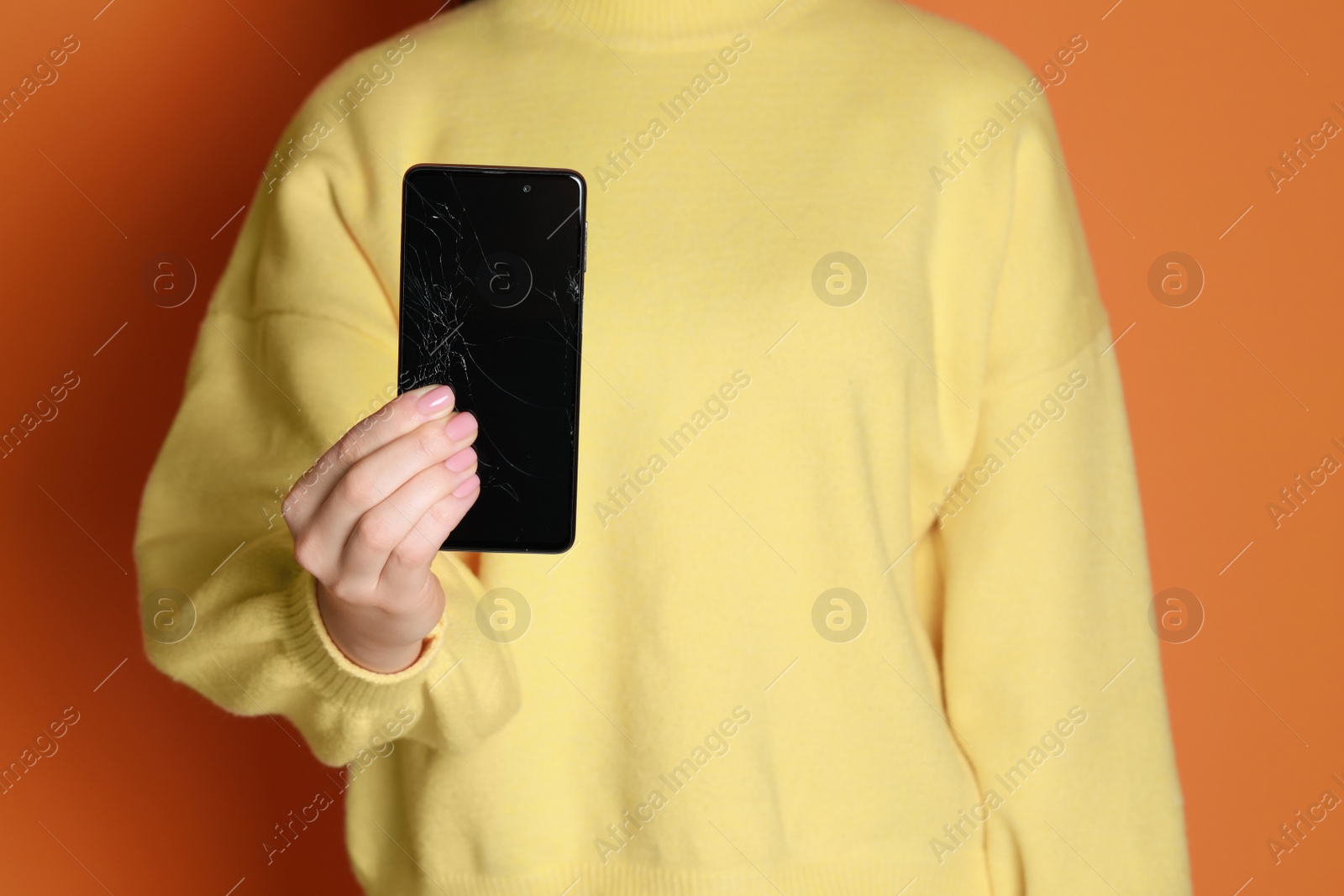 Photo of Woman showing damaged smartphone on orange background, closeup. Device repairing