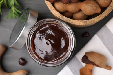 Photo of Jar of tasty tamarind sauce and fresh pods on grey wooden table, flat lay