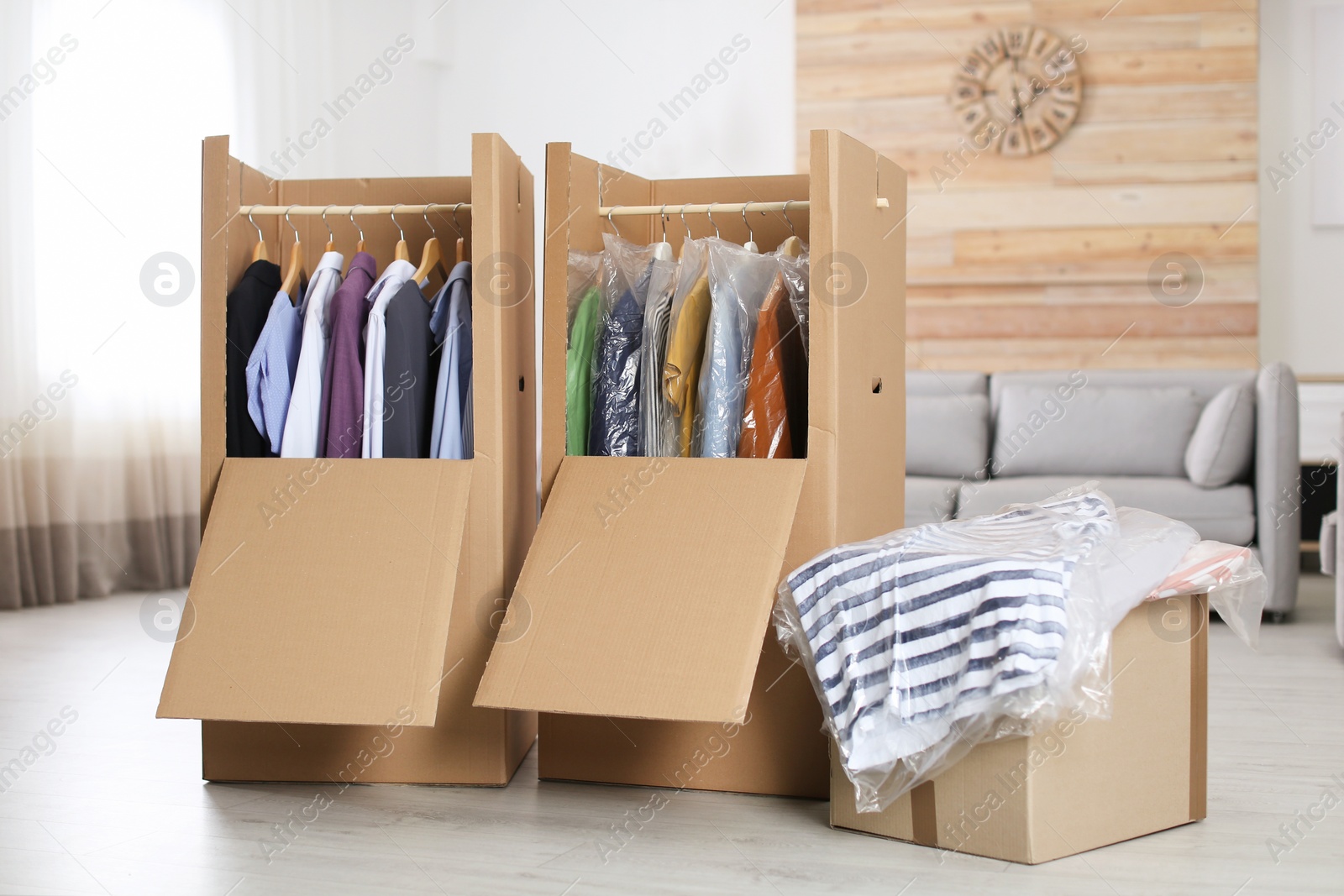 Photo of Cardboard wardrobe boxes with clothes on hangers in living room