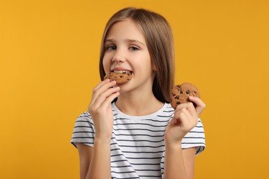 Photo of Cute girl eating chocolate chip cookies on orange background