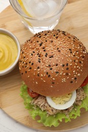 Photo of Delicious sandwich with tuna, boiled egg, vegetables served with mustard sauce and water with lemon on white table, above view