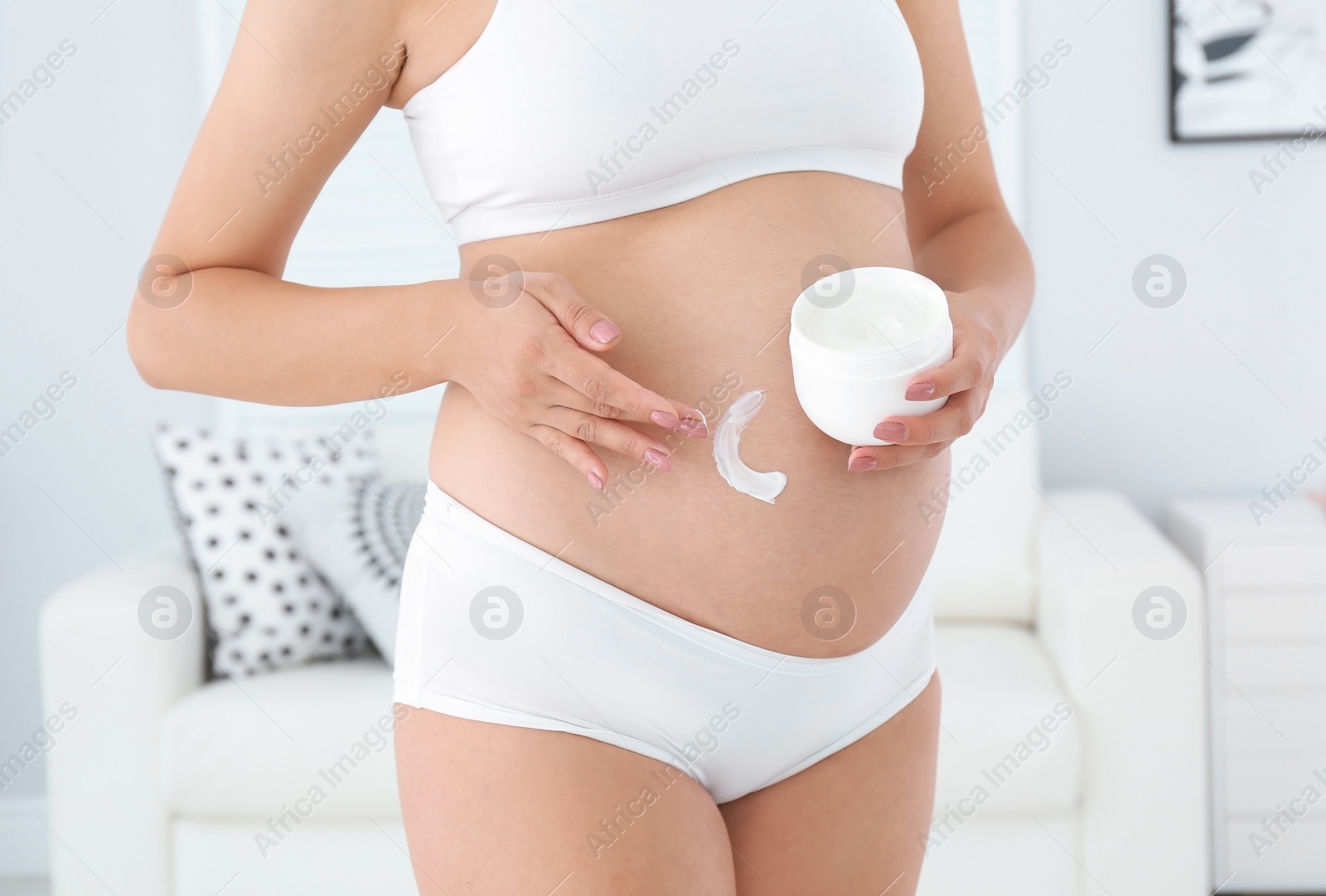 Photo of Pregnant woman applying body cream on belly at home, closeup