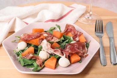 Photo of Fresh melon with prosciutto, mozzarella and arugula on wooden table