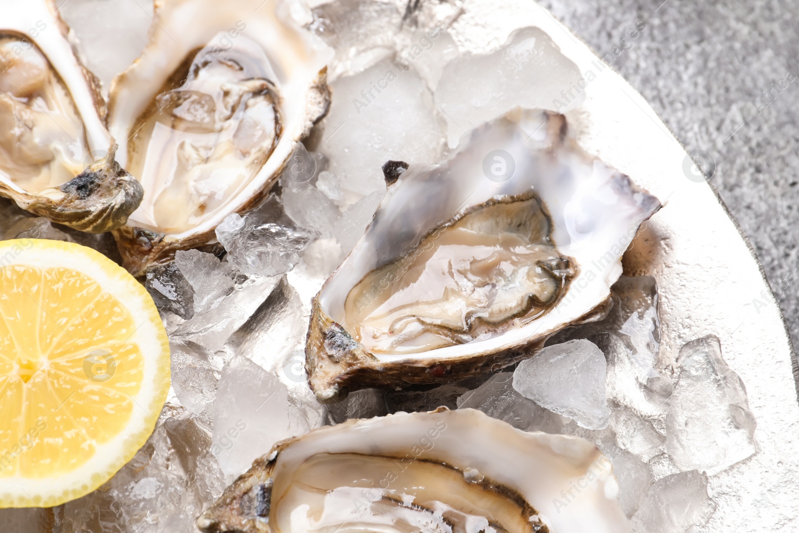 Photo of Delicious fresh oysters with lemon on grey table, closeup