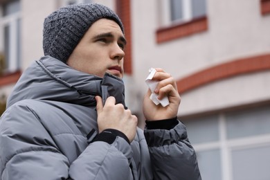 Photo of Sick young man with tissue on city street. Cold symptoms