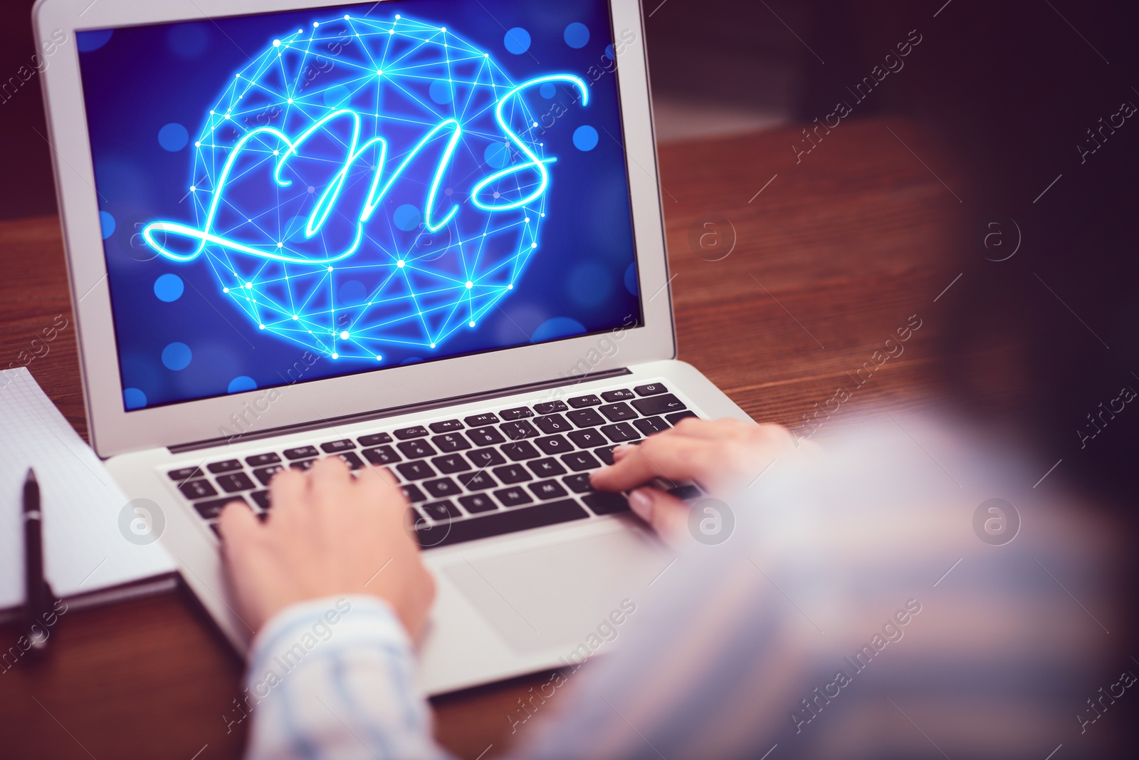 Image of Learning management system. Woman working with modern laptop at wooden table, closeup. Digital globe and abbreviation LMS on screen