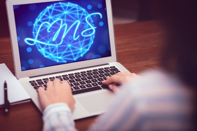 Image of Learning management system. Woman working with modern laptop at wooden table, closeup. Digital globe and abbreviation LMS on screen