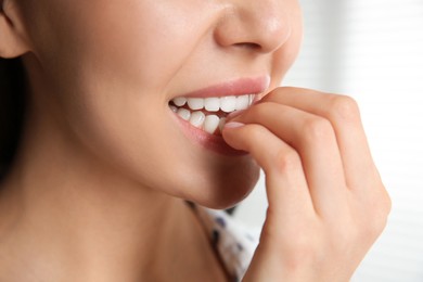 Young woman biting her nails on blurred background, closeup