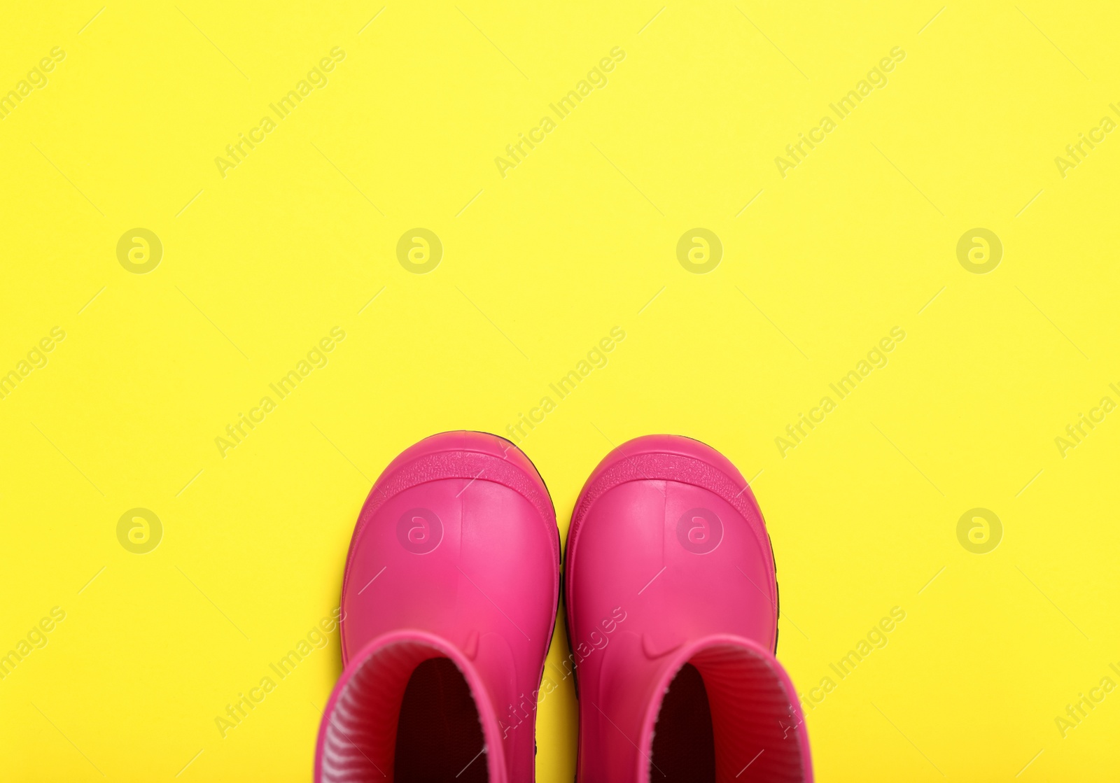 Photo of Pair of bright pink rubber boots on yellow background, top view. Space for text