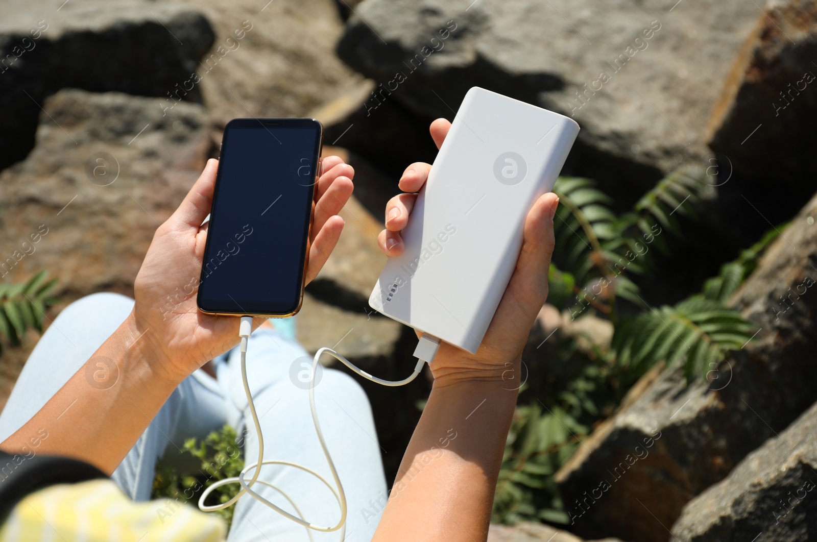 Photo of Woman charging smartphone with power bank on rocky mountain, closeup