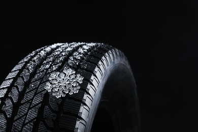 Winter tire with decorative snowflake on black background, closeup. Space for text