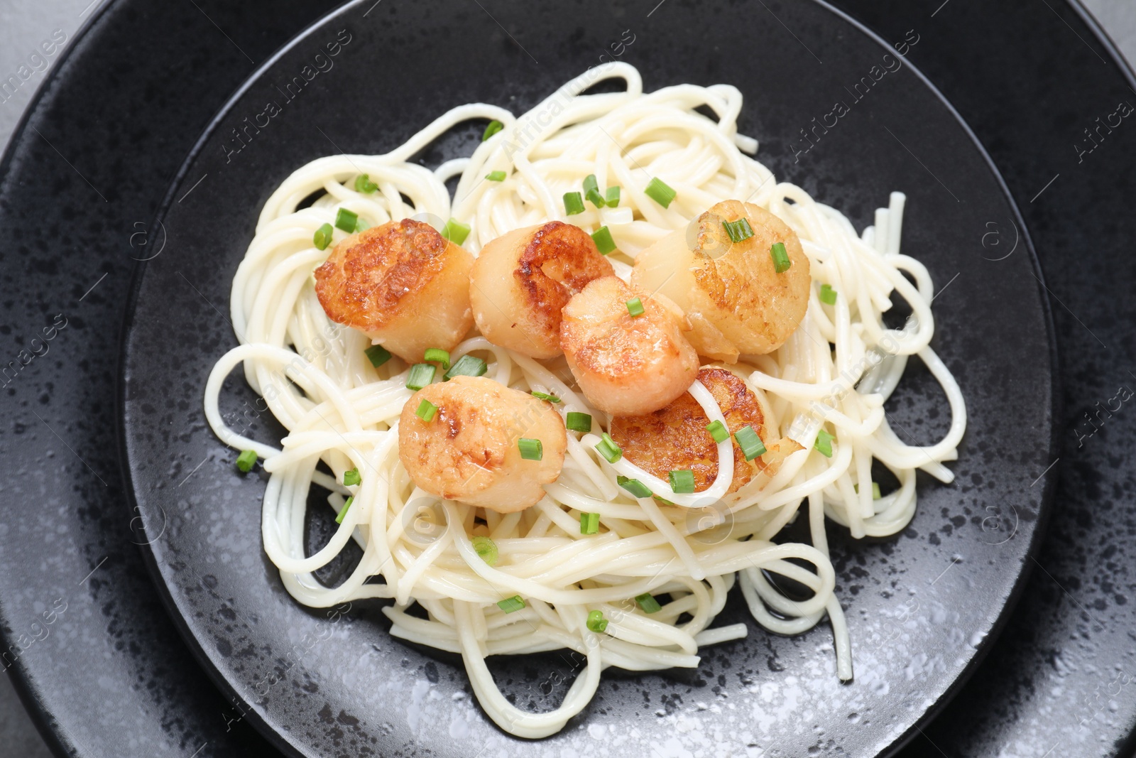 Photo of Delicious scallop pasta with green onion on plate, top view