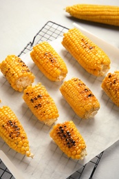 Photo of Cooling rack with grilled corn cobs on light background