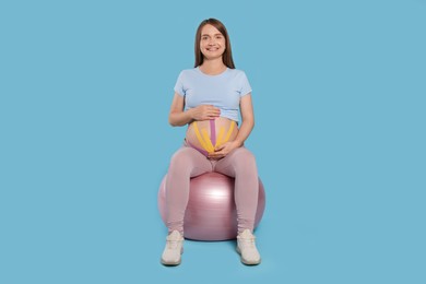 Photo of Beautiful pregnant woman with kinesio tapes doing exercises on fitball against light blue background