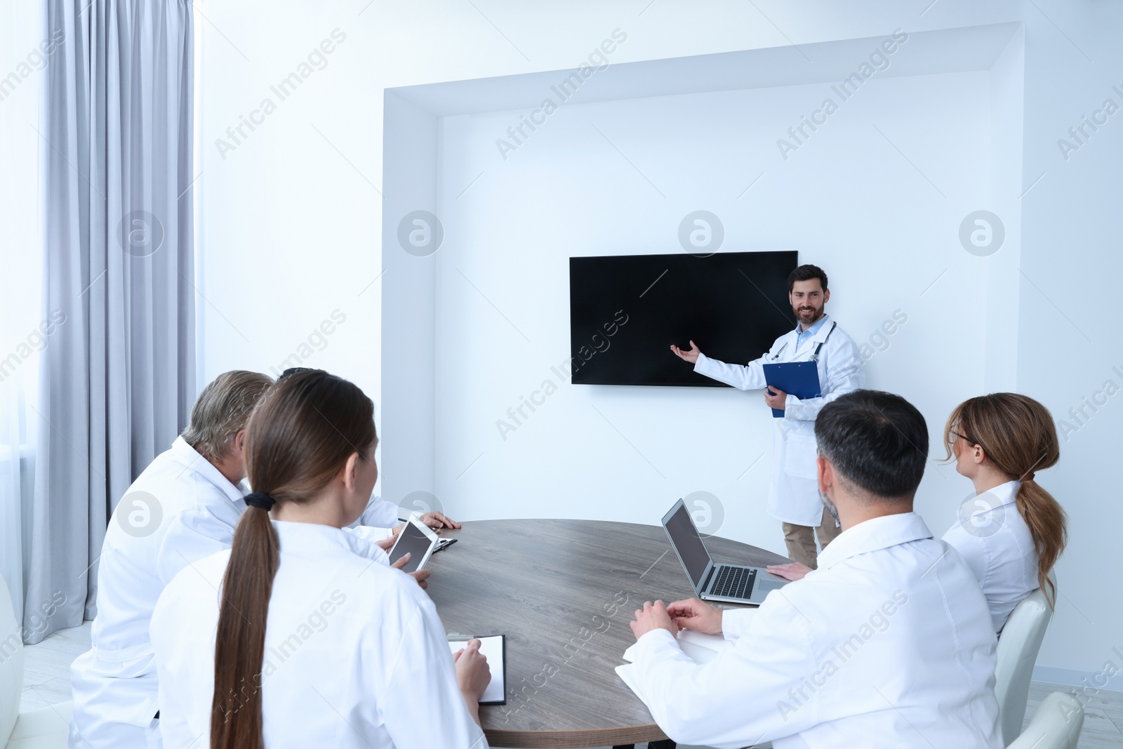 Photo of Team of doctors listening to speaker report near tv screen in meeting room. Medical conference