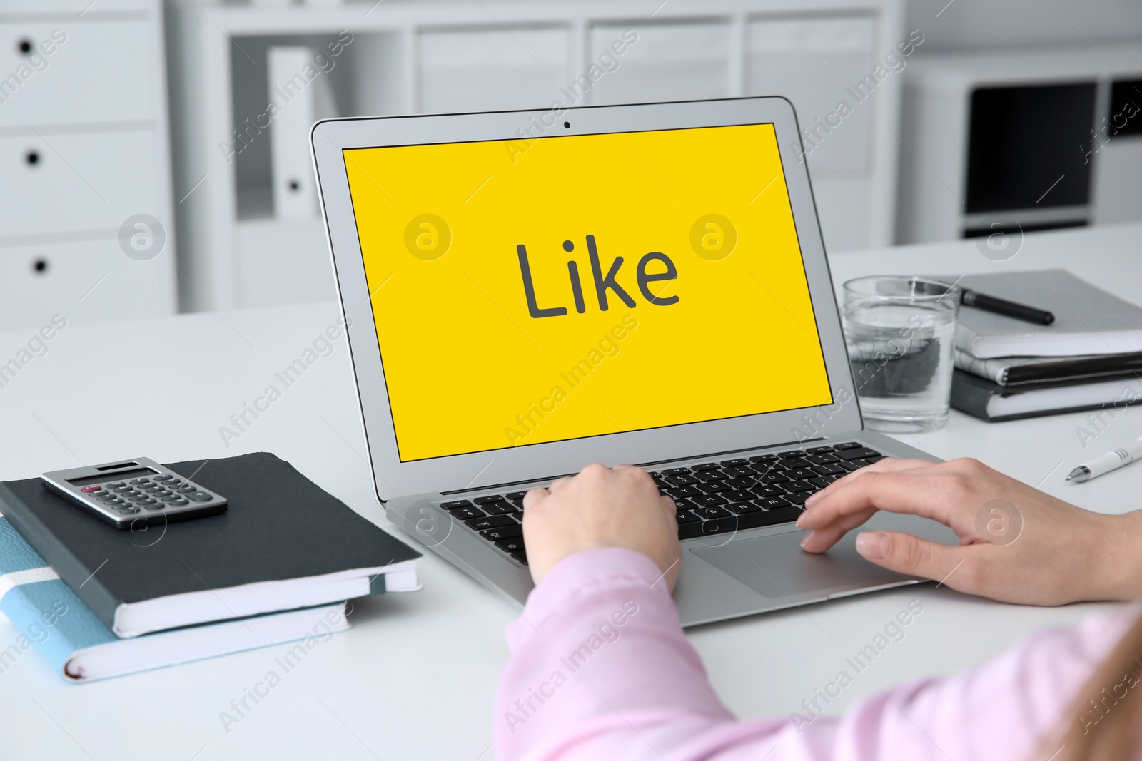 Image of Woman using laptop with word Like on screen at white table indoors, closeup