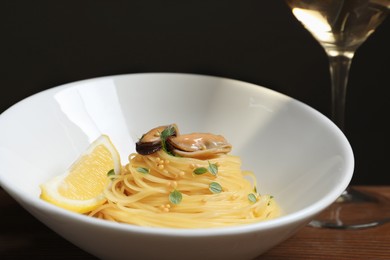 Photo of Tasty capellini with mussels and lemon on wooden table, closeup. Exquisite presentation of pasta dish