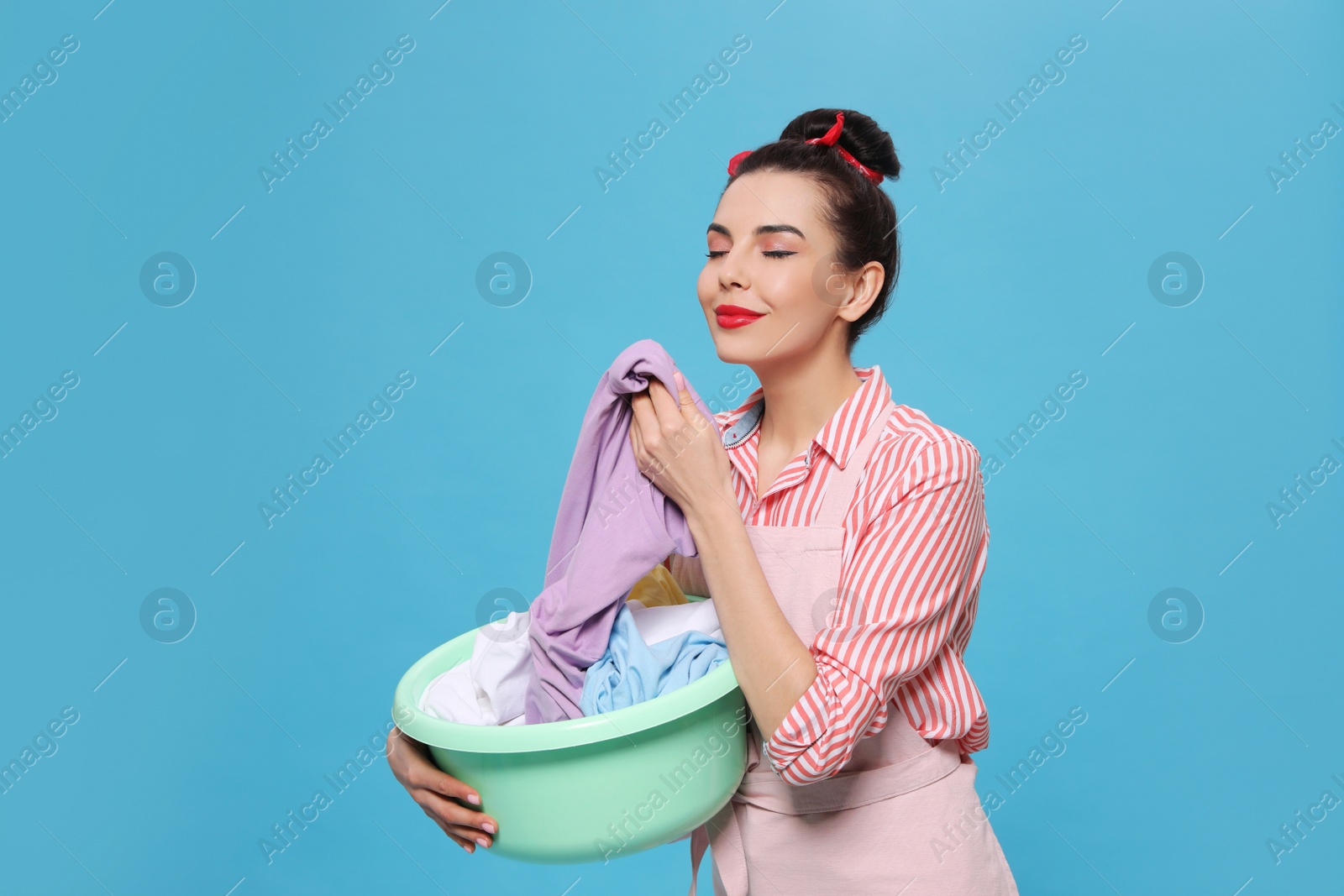 Photo of Housewife holding basin with clothes on light blue background