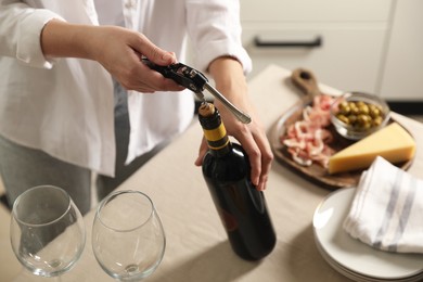 Woman opening wine bottle with corkscrew at table indoors, closeup