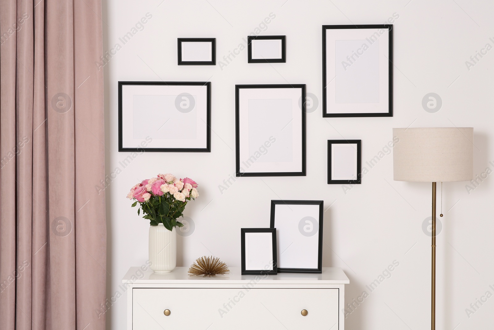 Photo of Empty frames hanging on white wall and chest of drawers with flowers indoors