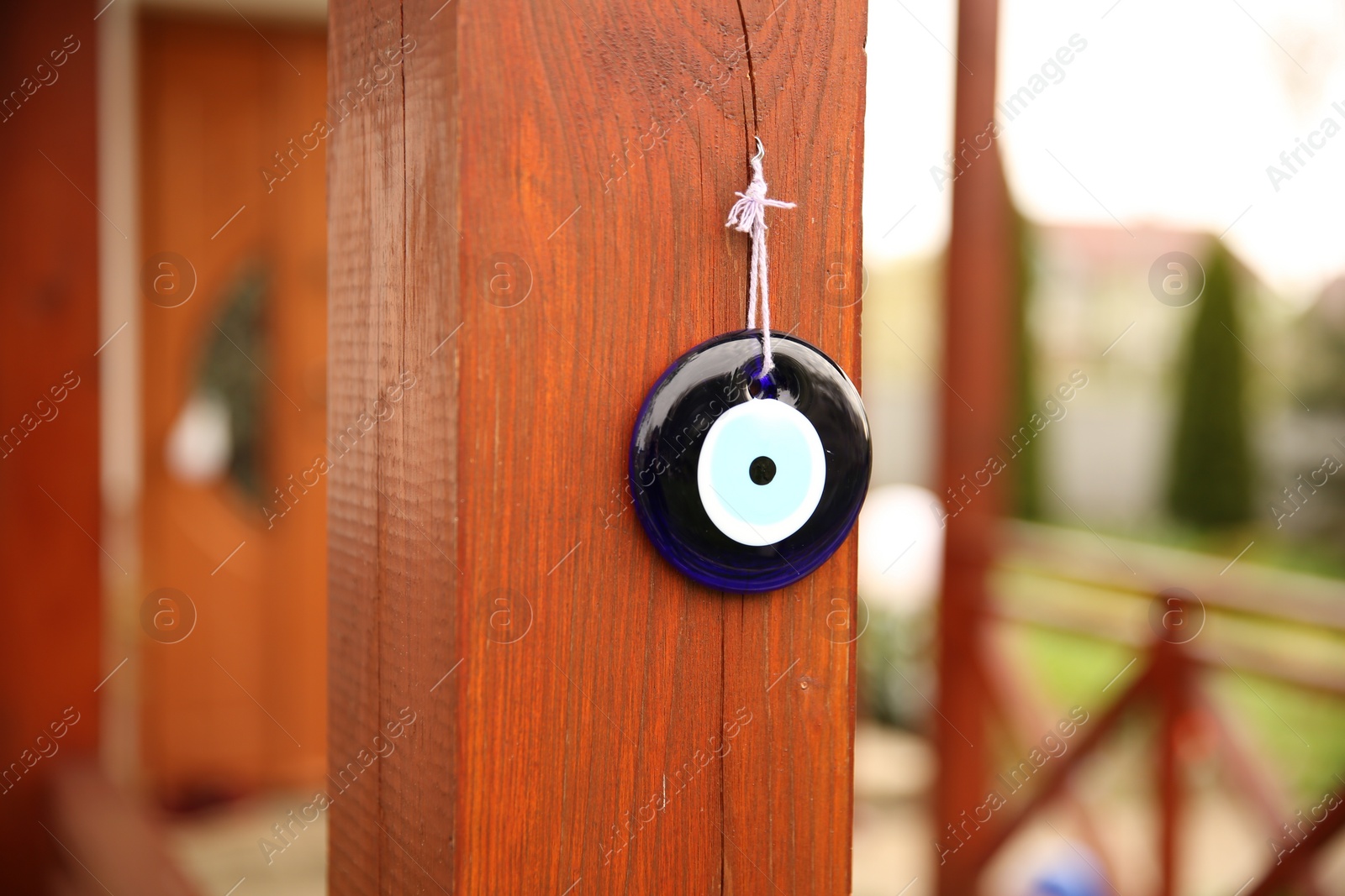 Photo of Evil eye amulet hanging on wooden pillar outdoors, closeup