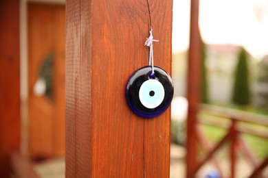 Evil eye amulet hanging on wooden pillar outdoors, closeup