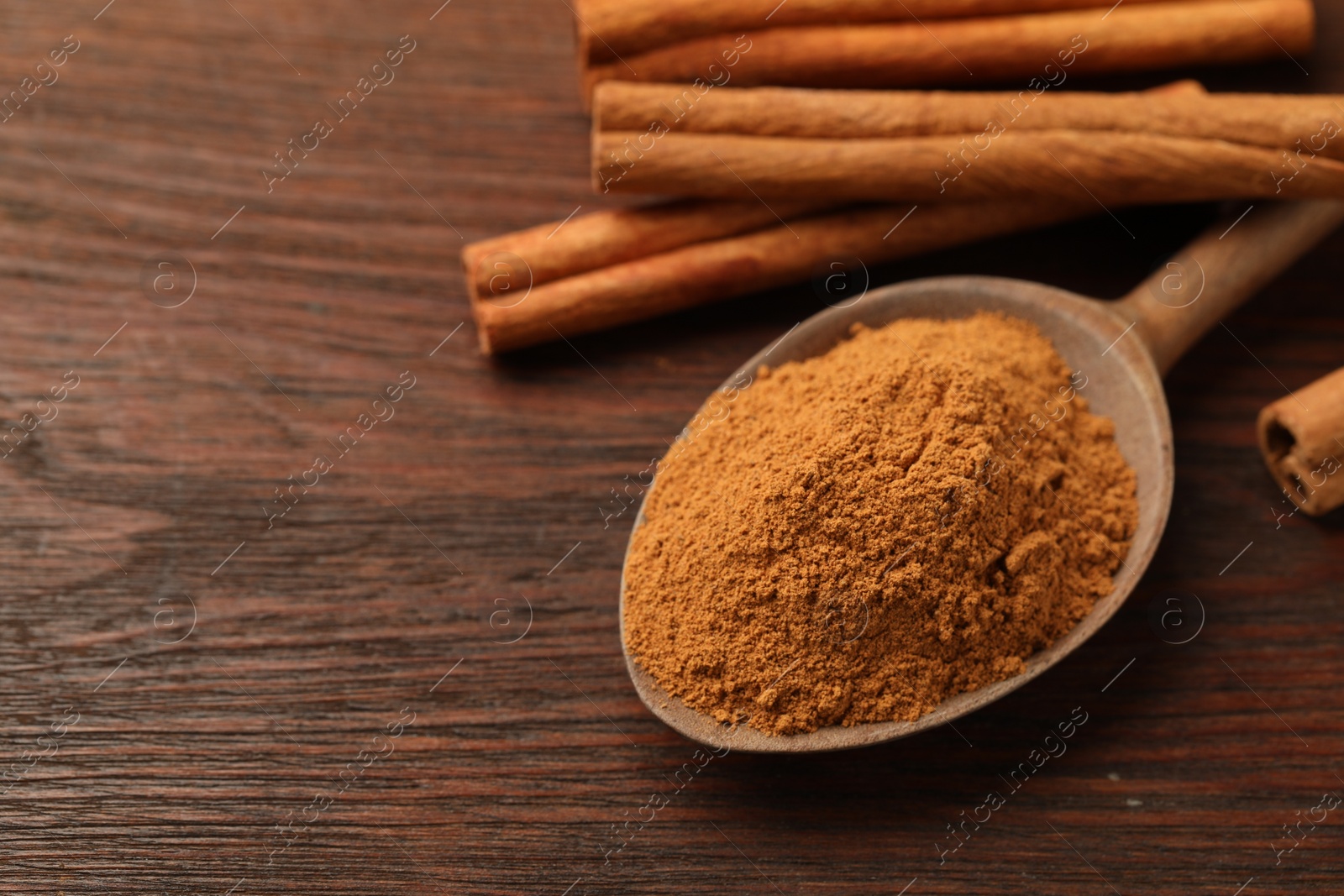 Photo of Spoon with cinnamon powder and sticks on wooden table, closeup. Space for text