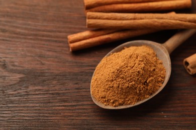 Photo of Spoon with cinnamon powder and sticks on wooden table, closeup. Space for text