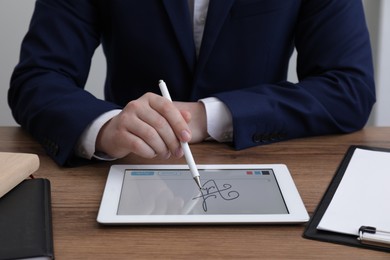 Electronic signature. Man using stylus and tablet at wooden table, closeup