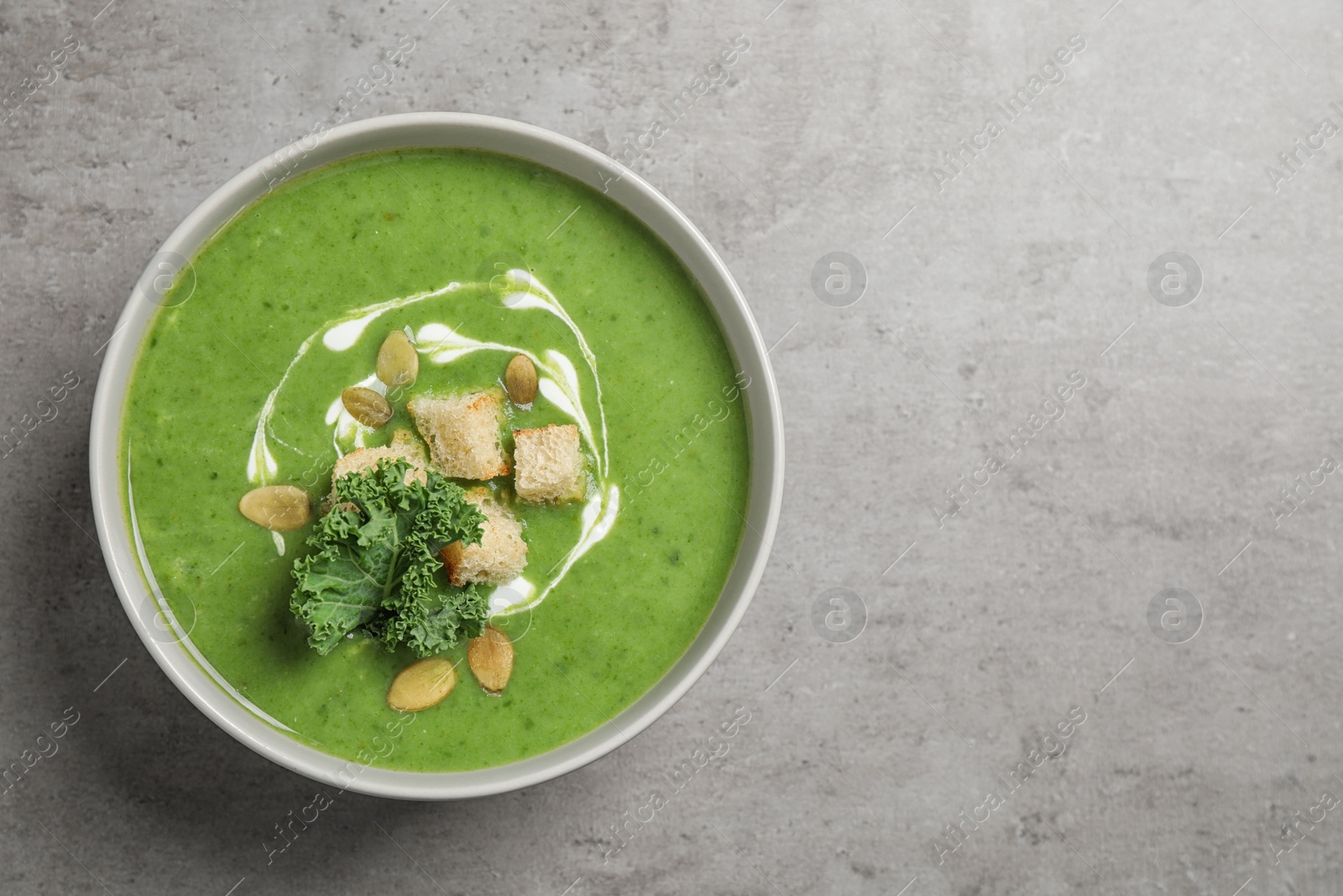 Photo of Tasty kale soup with croutons on grey table, top view. Space for text