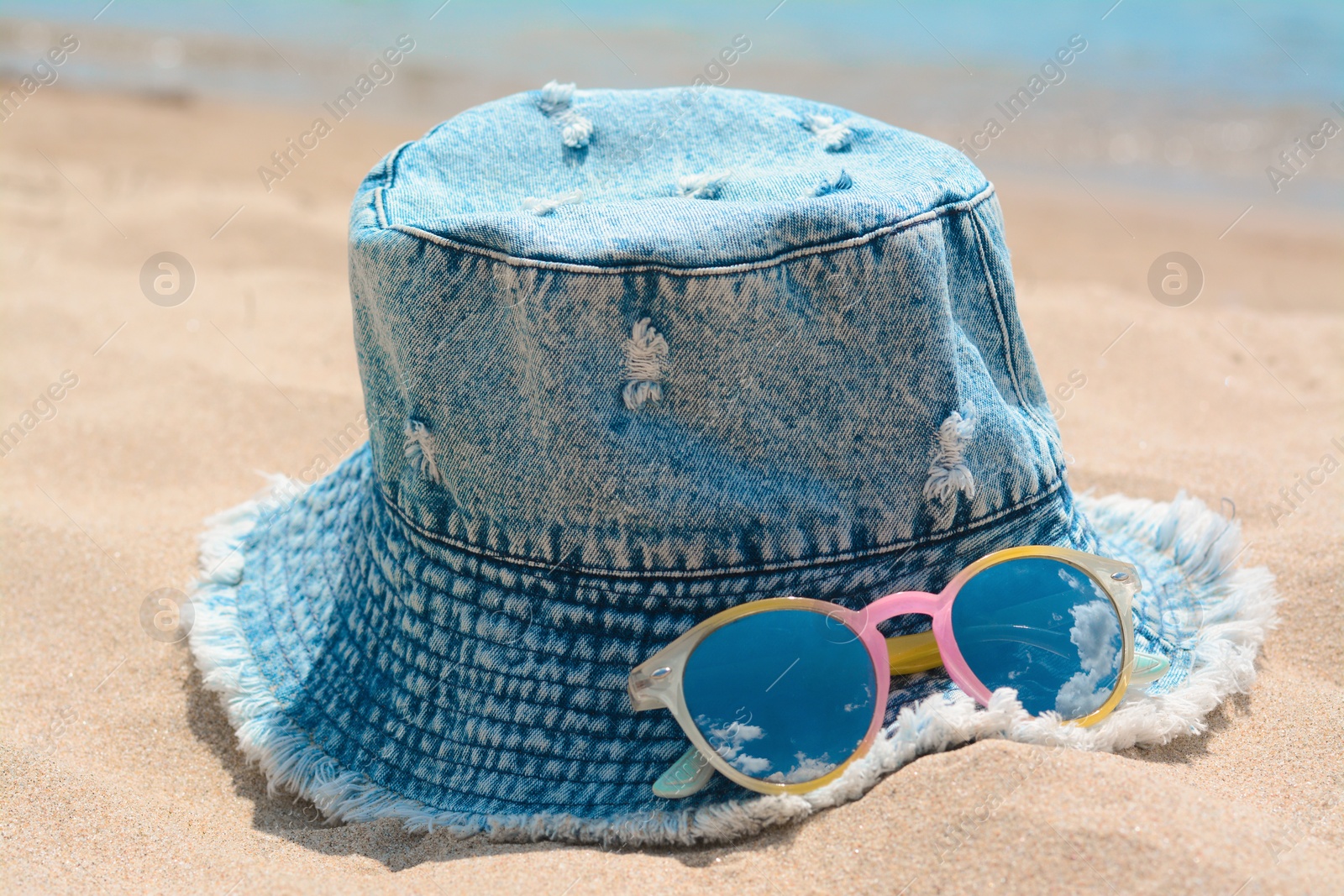 Photo of Jeans hat and sunglasses on sand, closeup. Beach accessories