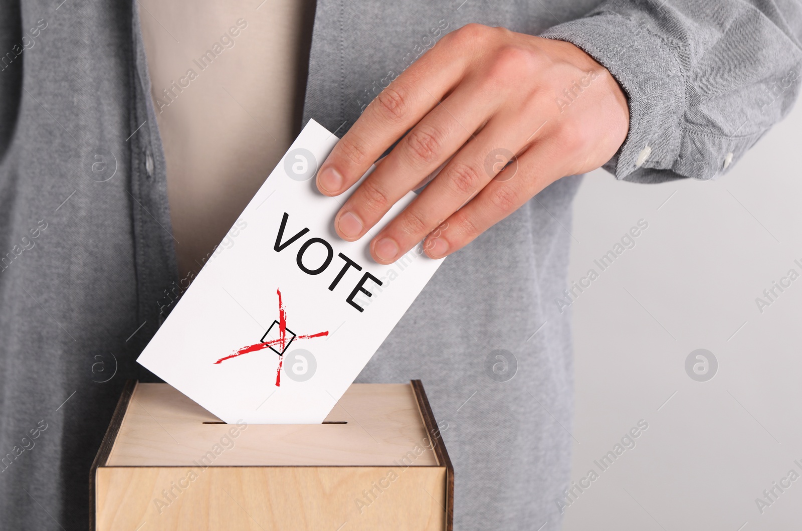 Image of Man putting paper with word Vote and tick into ballot box on light grey background