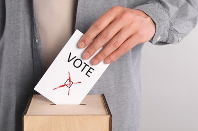 Man putting paper with word Vote and tick into ballot box on light grey background