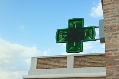Green cross sign of drugstore on building wall against blue sky