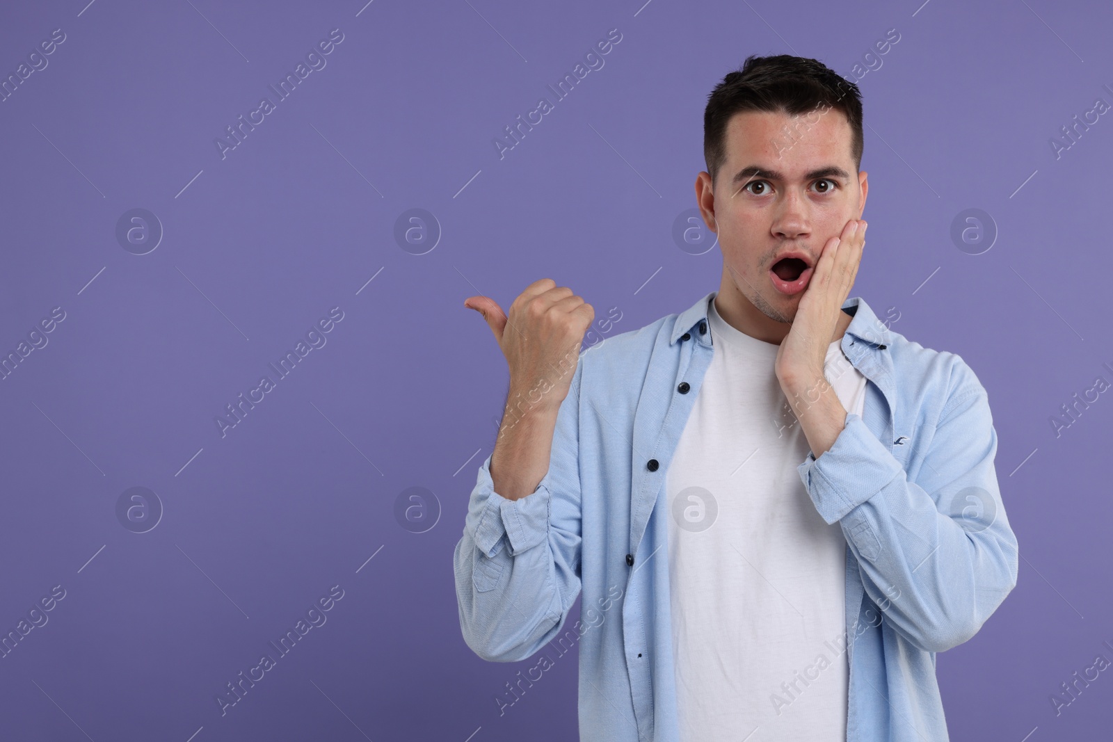 Photo of Special promotion. Emotional man pointing at something on violet background, space for text