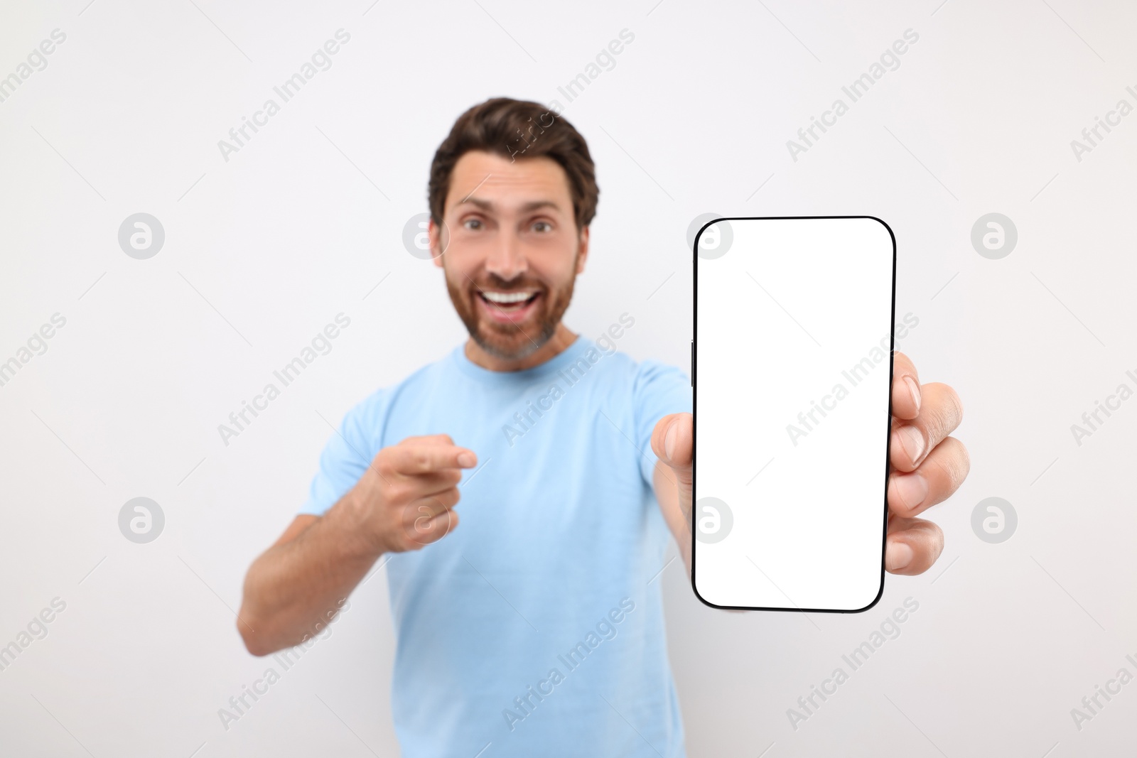 Photo of Handsome man showing smartphone in hand and pointing at it on white background, selective focus. Mockup for design