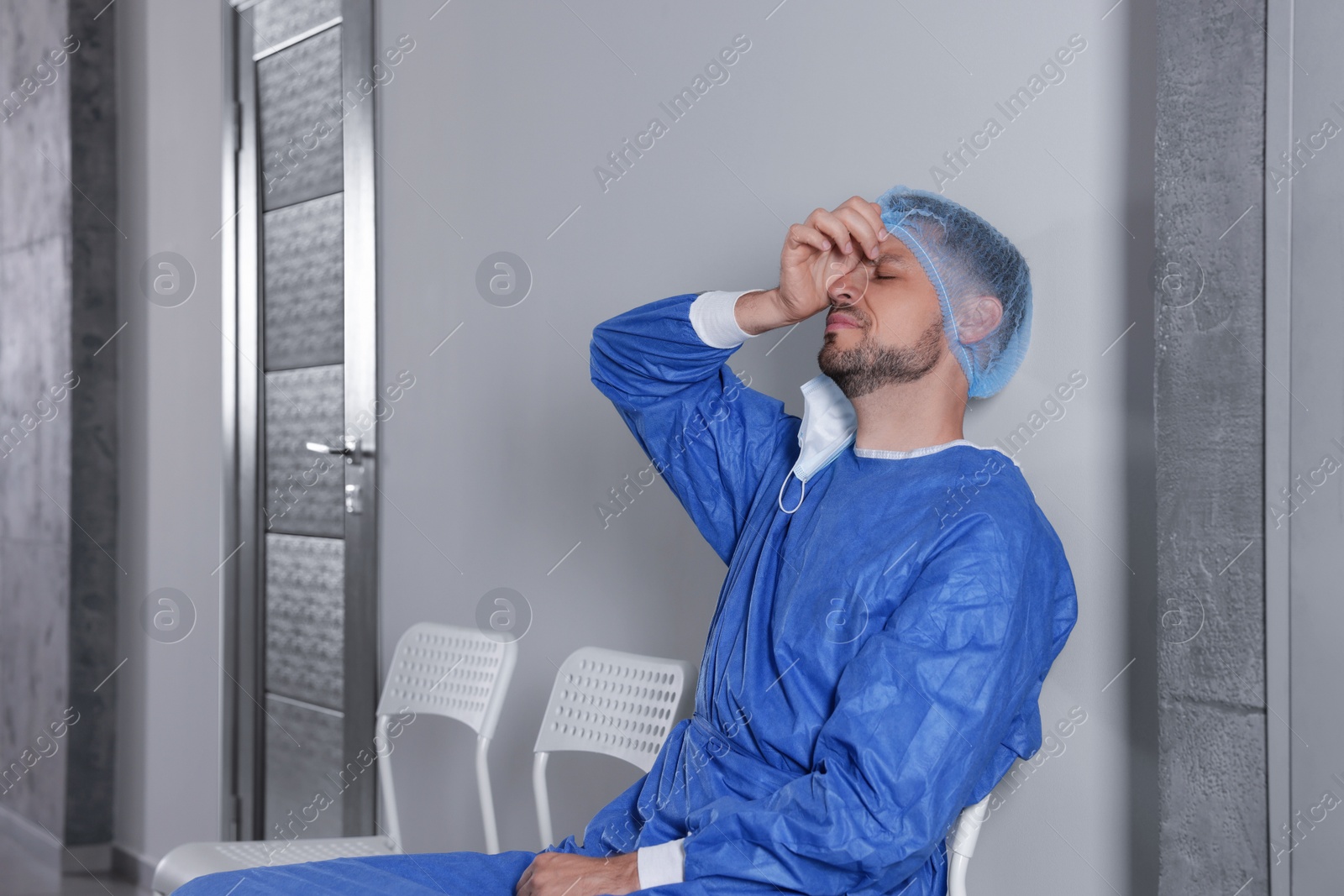 Photo of Exhausted doctor sitting on chair in hospital corridor, space for text