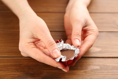 Photo of Woman unwrapping heart shaped chocolate candy at wooden table, closeup