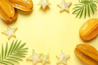 Carambola fruits and leaves on yellow background, flat lay. Space for text