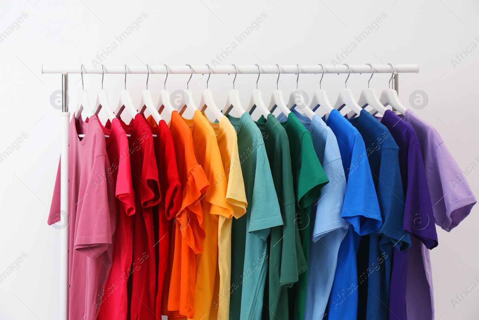 Photo of Rack with bright clothes on white background. Rainbow colors