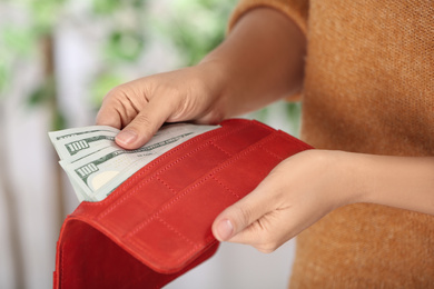 Woman putting money into wallet on blurred background, closeup