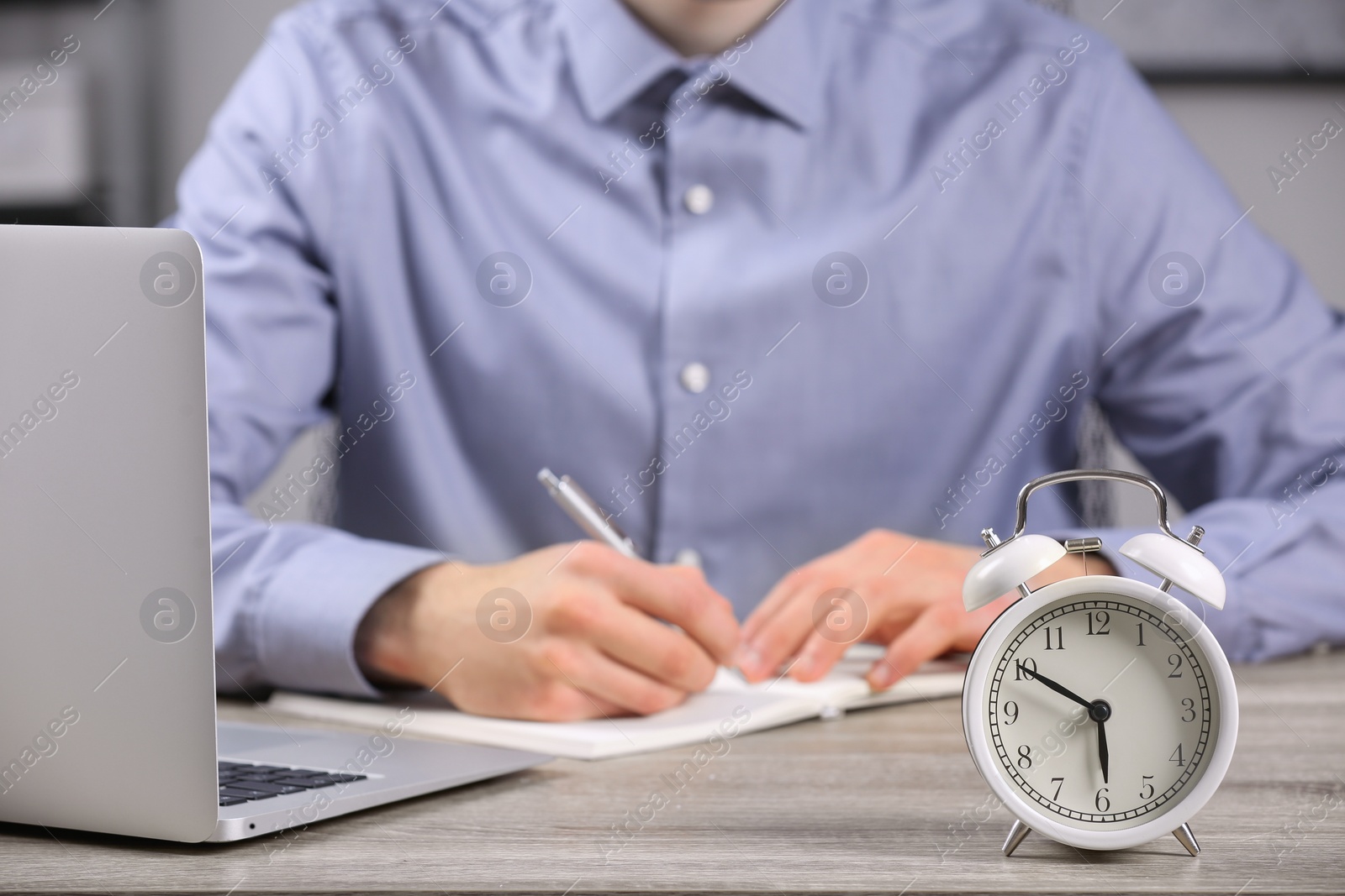 Photo of White alarm clock and man working at wooden table, closeup