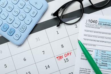 Photo of Tax day. Calendar with date reminder, document, pen, glasses and calculator on table, flat lay